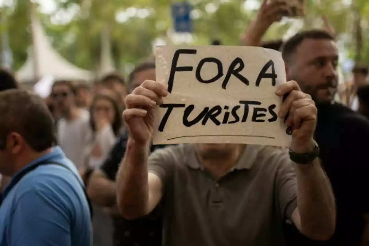 Persona sostiene un cartel con el mensaje Fora Turistes en una manifestación rodeada de más gente. Persona sostiene un cartel con el mensaje Fora Turistes en una manifestación rodeada de más gente.