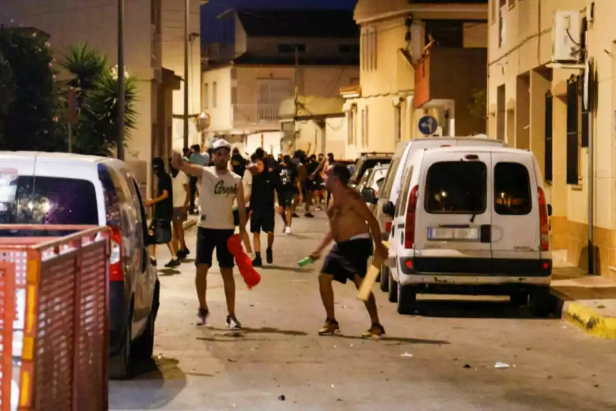 Grupo de personas en una calle durante la noche, algunas de ellas parecen estar en una situación de disturbio o enfrentamiento Grupo de personas en una calle durante la noche, algunas de ellas parecen estar en una situación de disturbio o enfrentamiento