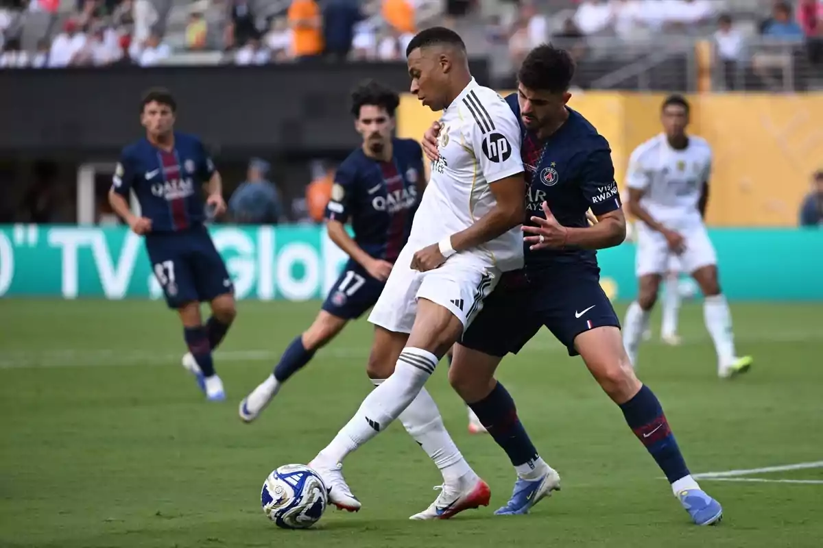 Dos futbolistas disputan el balón durante un partido entre Real Madrid y PSG mientras otros jugadores observan la jugada en el fondo del campo. Dos futbolistas disputan el balón durante un partido entre Real Madrid y PSG mientras otros jugadores observan la jugada en el fondo del campo.