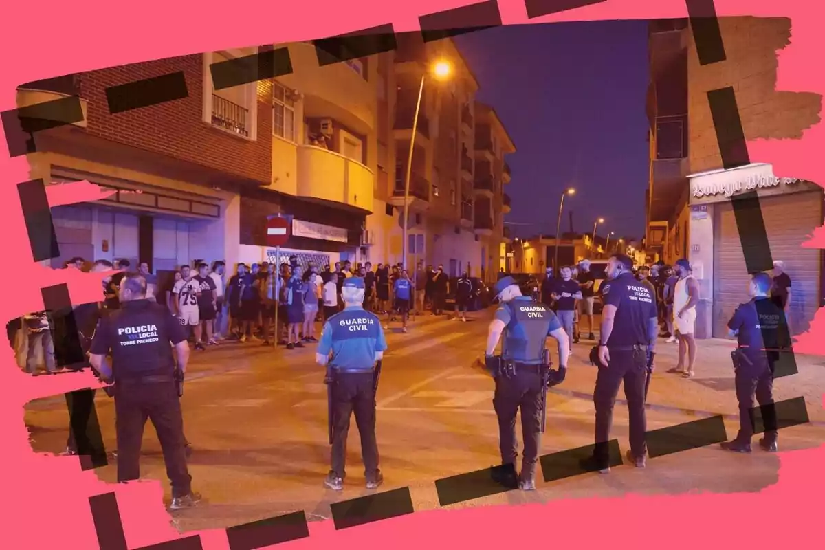 Un grupo de policías y guardias civiles forman una barrera frente a un grupo de personas en una calle de noche, con edificios residenciales y luces encendidas, todo enmarcado por un borde rosa con líneas negras.