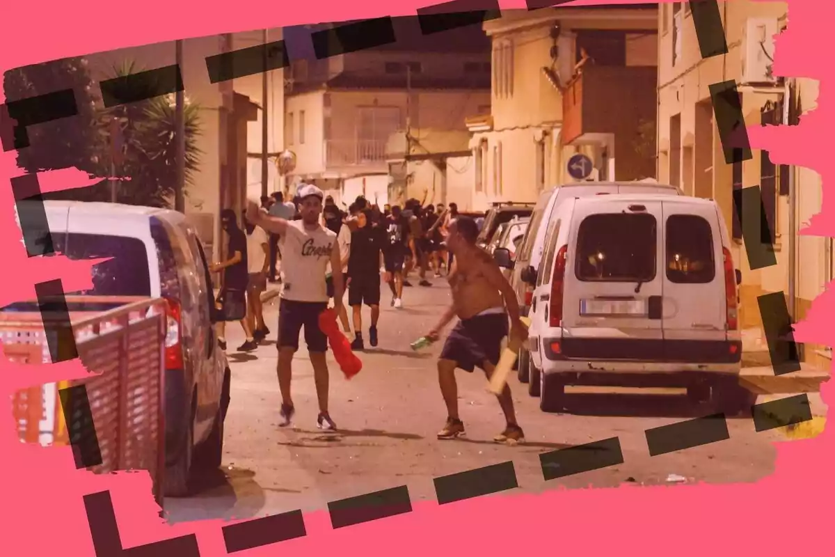 Grupo de personas en una calle durante la noche, algunas parecen estar discutiendo o peleando, rodeados de coches estacionados y con un marco decorativo rosa