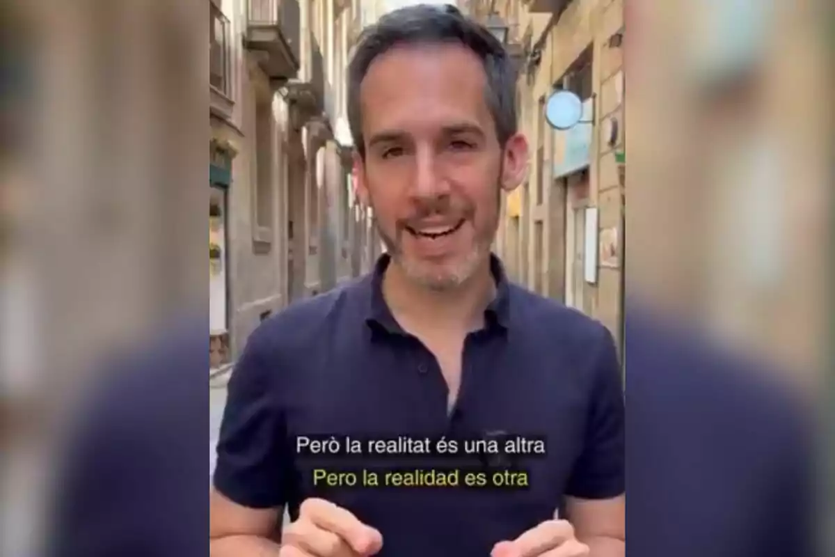 Hombre de cabello corto y barba hablando en una calle estrecha con subtítulos en catalán y español que dicen Pero la realidad es otra