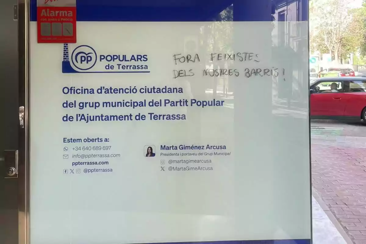 Puerta de cristal de la oficina del Partido Popular de Terrassa con información de contacto y un mensaje escrito a mano que dice Puerta de cristal de la oficina del Partido Popular de Terrassa con información de contacto y un mensaje escrito a mano que dice