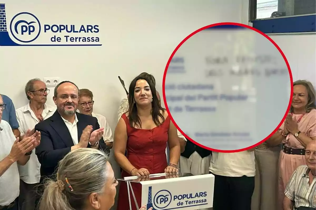 Un grupo de personas aplaude en un evento del Partido Popular de Terrassa, con una mujer en el centro detrás de un atril y el logo del partido en la pared.