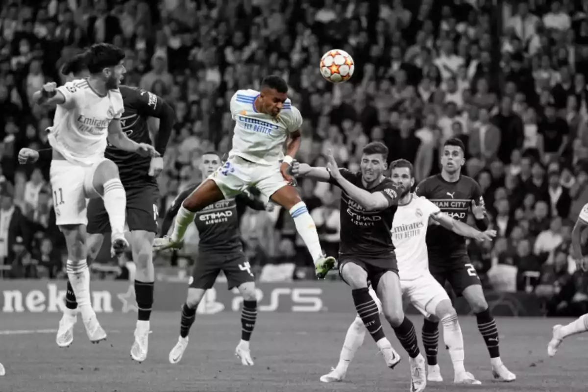 Un jugador de fútbol salta para rematar de cabeza un balón durante un partido importante mientras otros jugadores lo rodean y el fondo está en blanco y negro excepto el jugador y el balón que están a color Un jugador de fútbol salta para rematar de cabeza un balón durante un partido importante mientras otros jugadores lo rodean y el fondo está en blanco y negro excepto el jugador y el balón que están a color