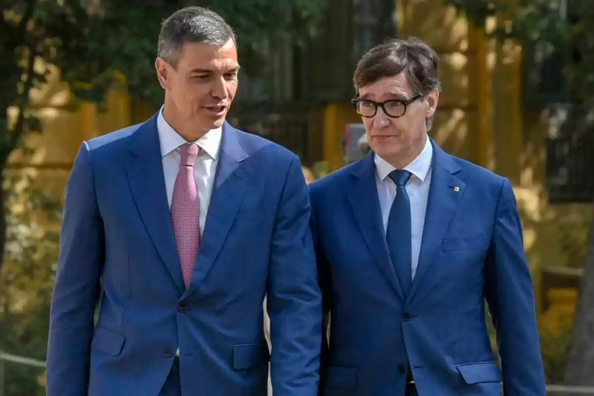 Dos hombres vestidos con traje azul caminan juntos al aire libre mientras conversan
