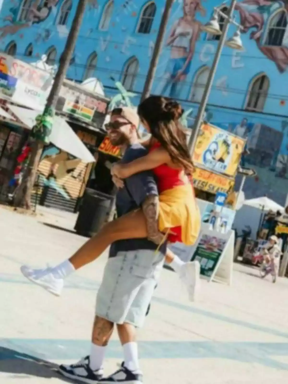 Pareja joven disfrutando de un paseo en Venice Beach mientras él carga a ella en su espalda y ambos sonríen Pareja joven disfrutando de un paseo en Venice Beach mientras él carga a ella en su espalda y ambos sonríen