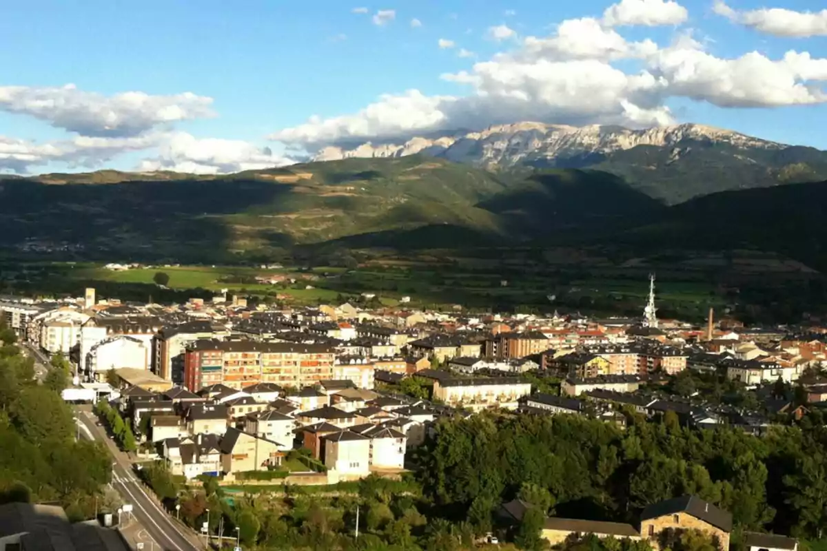 Vista panorámica de una ciudad rodeada de montañas verdes bajo un cielo azul con nubes blancas Vista panorámica de una ciudad rodeada de montañas verdes bajo un cielo azul con nubes blancas