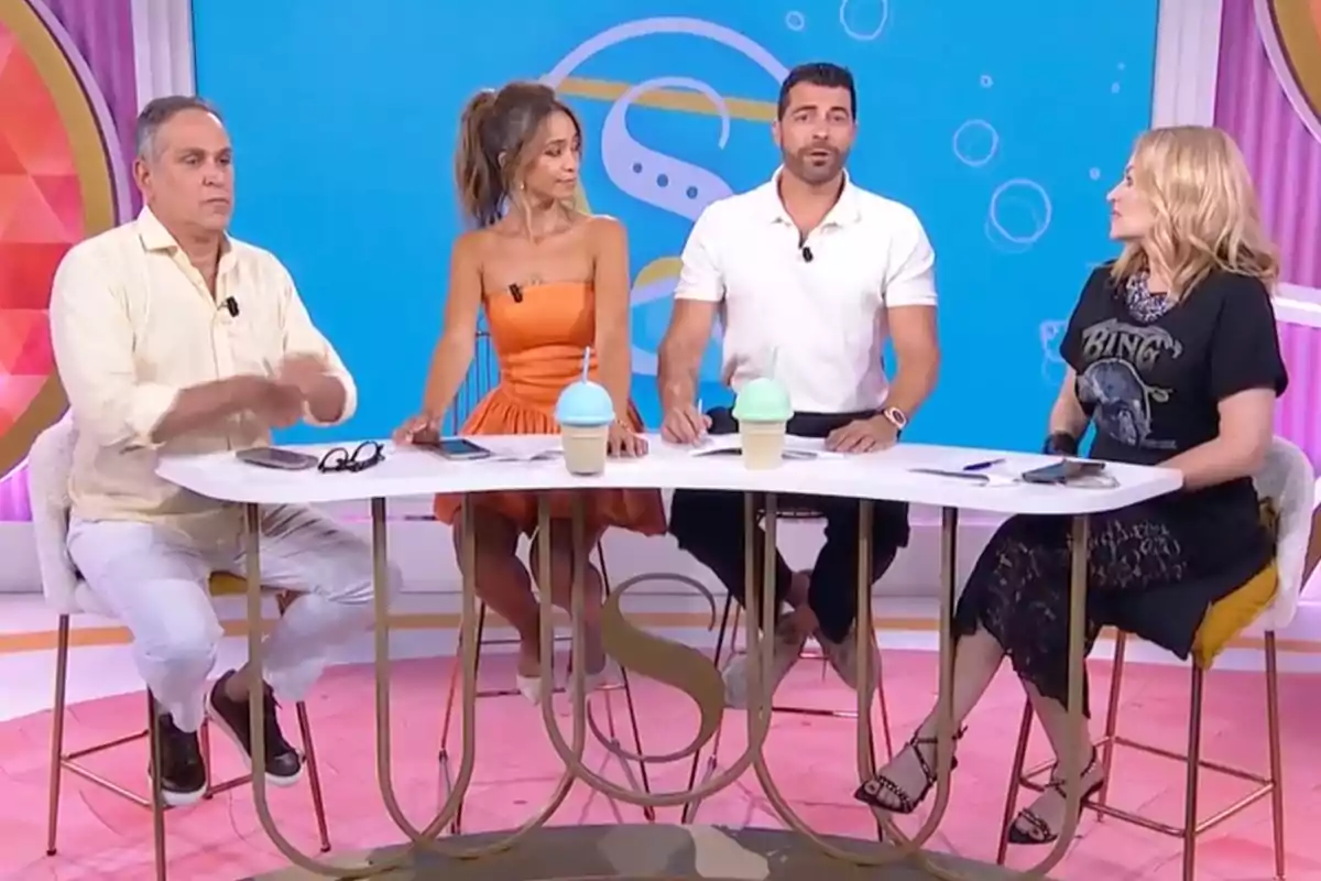 Cuatro personas sentadas alrededor de una mesa en un set de televisión colorido, con bebidas y objetos personales sobre la mesa, todos conversando y mirando en diferentes direcciones. Captura de 'Socialité' Cuatro personas sentadas alrededor de una mesa en un set de televisión colorido, con bebidas y objetos personales sobre la mesa, todos conversando y mirando en diferentes direcciones. Captura de 'Socialité'