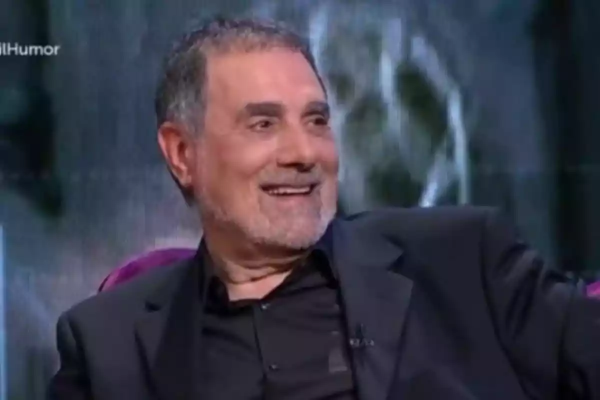 Toni Cruz de cabello canoso y barba corta sonriendo mientras está sentado en un programa de televisión Toni Cruz de cabello canoso y barba corta sonriendo mientras está sentado en un programa de televisión