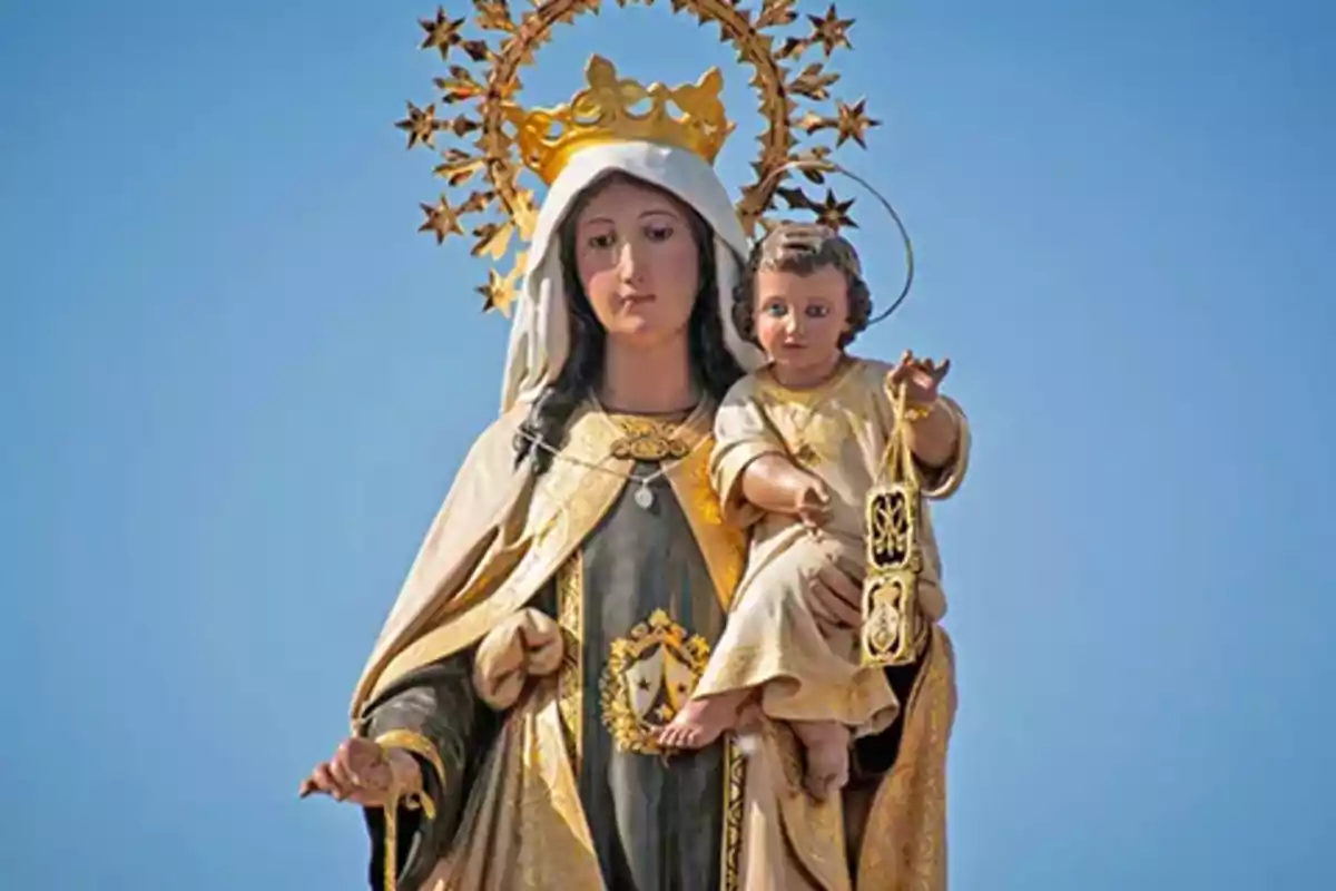 Escultura religiosa de una virgen con corona dorada sosteniendo al niño Jesús bajo un cielo azul