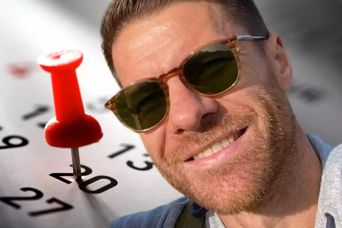 Hombre sonriente con gafas de sol frente a un calendario marcado con una chincheta roja en el día 20