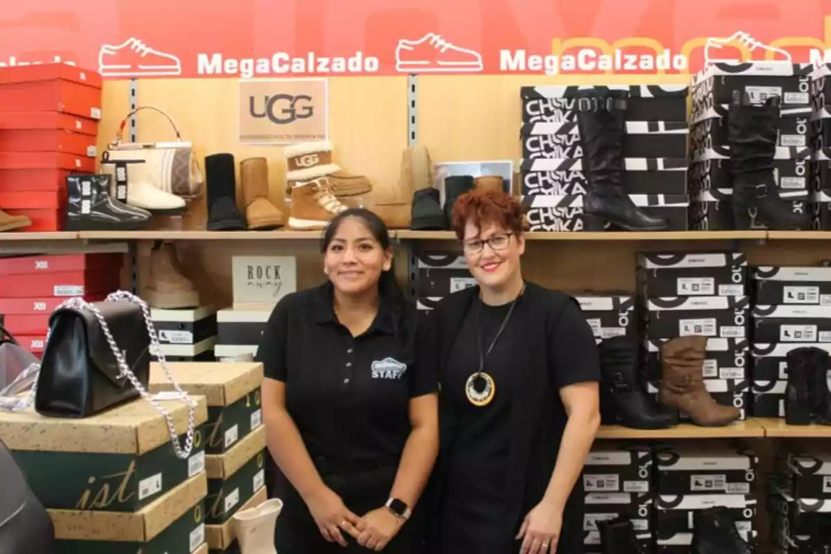 Dos personas posando en una tienda de calzado con varias cajas y botas en exhibición.