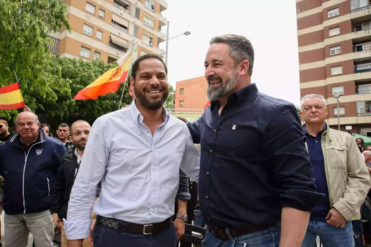 Plano medio de Ignacio Garriga y Santiago Abascal riendo en una plaza de Salt con decenas de simpatizantes detrás