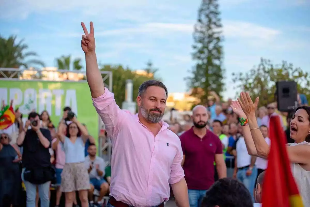 Plano medio de Santiago Abascal con el brazo derecho en alto haciendo el gesto de la V con los dedos