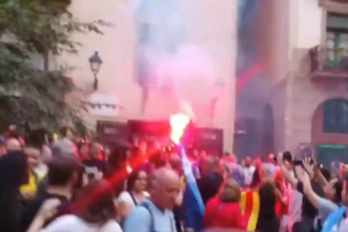 Una multitud de personas en una manifestación con bengalas y banderas en una calle.