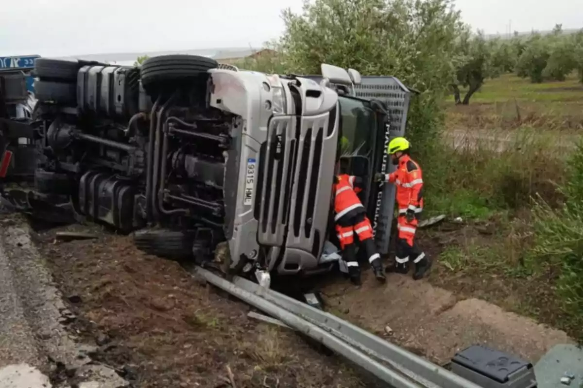 Un camión volcado en la carretera con dos personas de rescate trabajando en la escena.