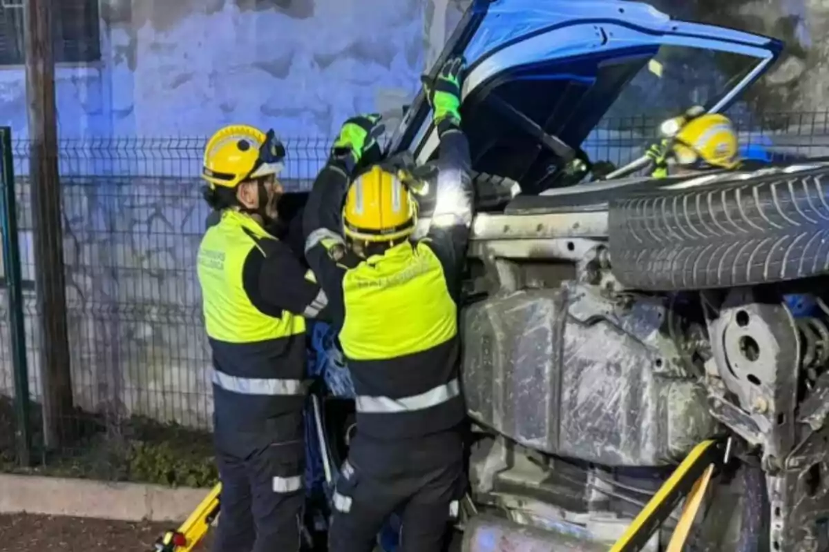 Dos bomberos con cascos amarillos y chalecos reflectantes trabajan en un vehículo volcado.