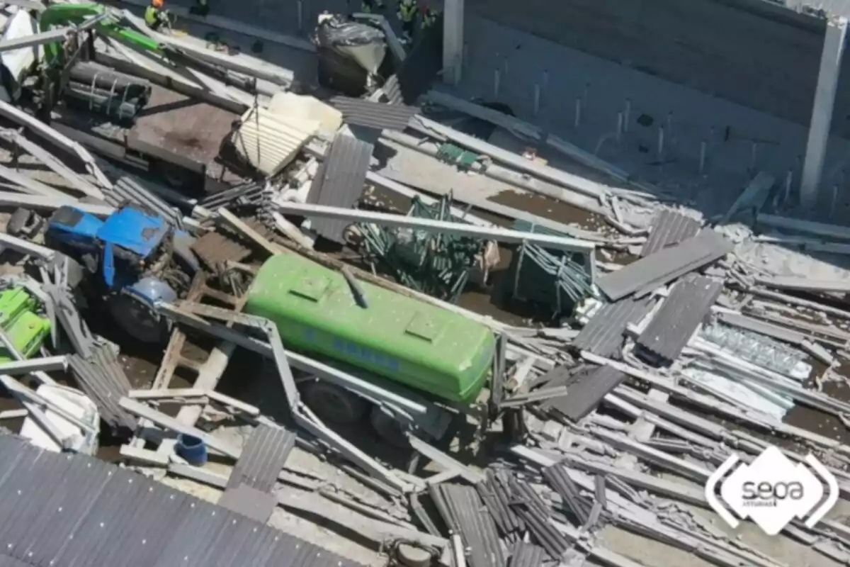Vista aérea de un colapso estructural en una nave industrial con escombros de metal y vehículos atrapados entre los restos Vista aérea de un colapso estructural en una nave industrial con escombros de metal y vehículos atrapados entre los restos