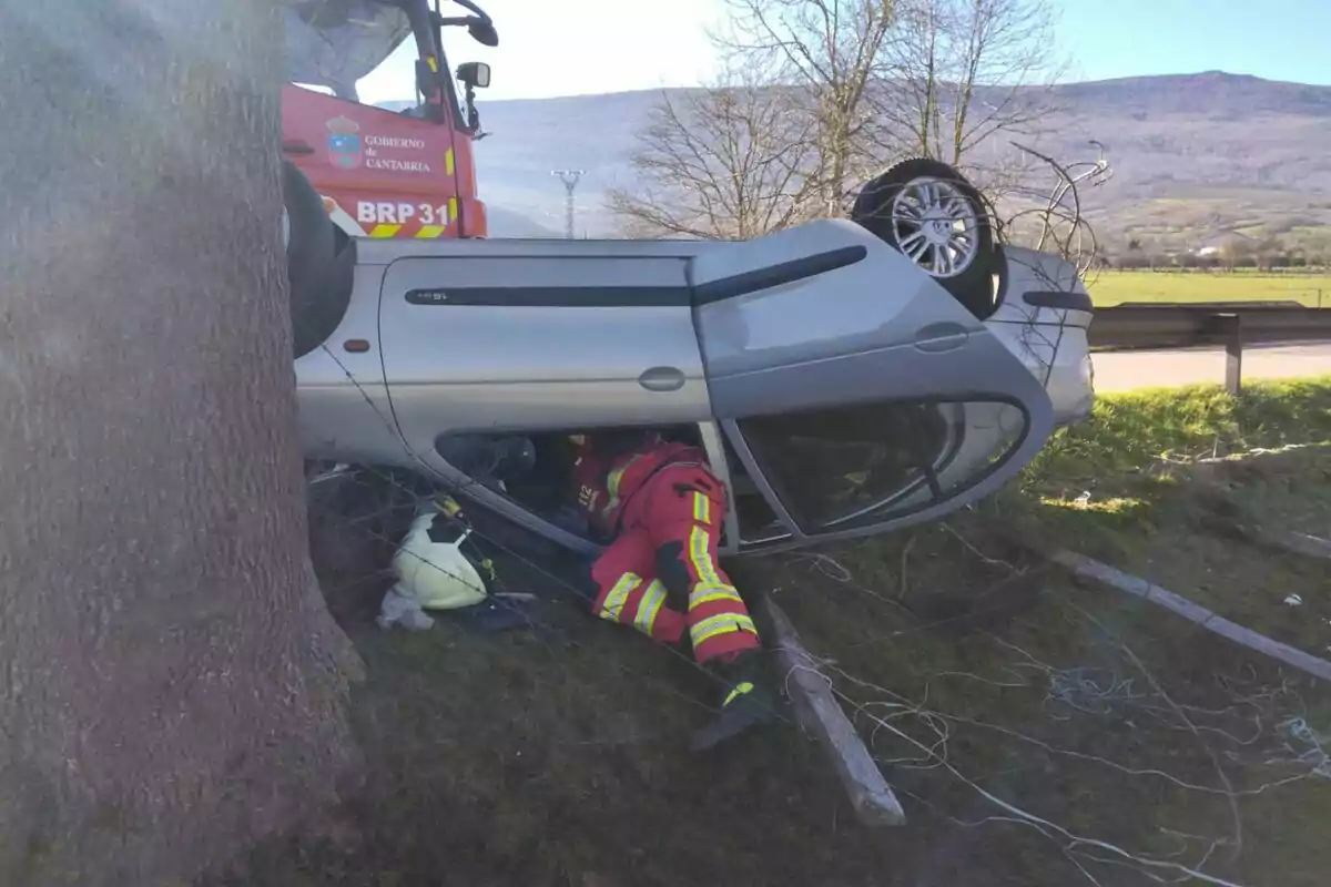 Un coche volcado en una zona rural con un bombero trabajando en el rescate.