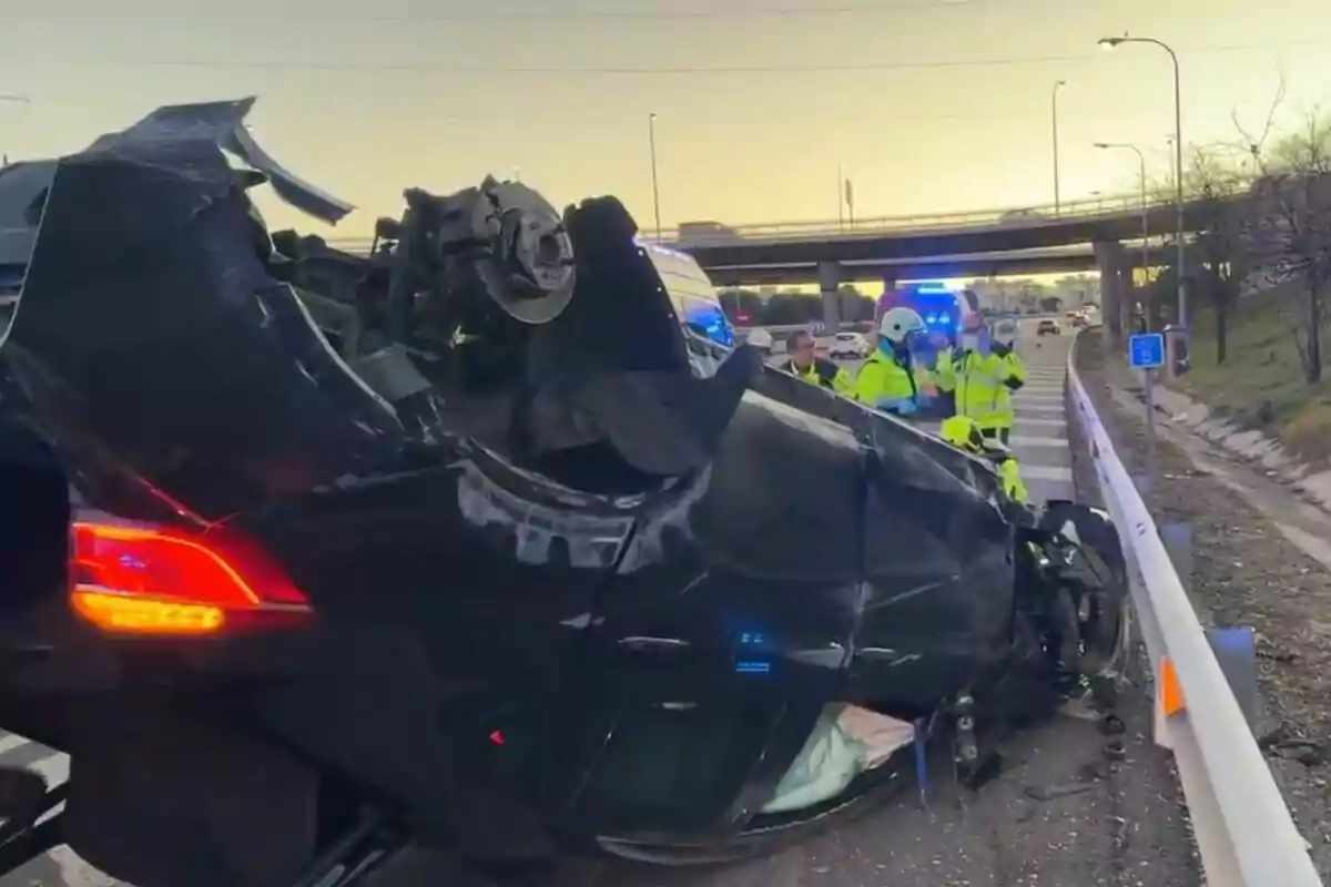 Un coche volcado en una carretera con varios agentes de emergencia alrededor y luces de vehículos de emergencia encendidas.