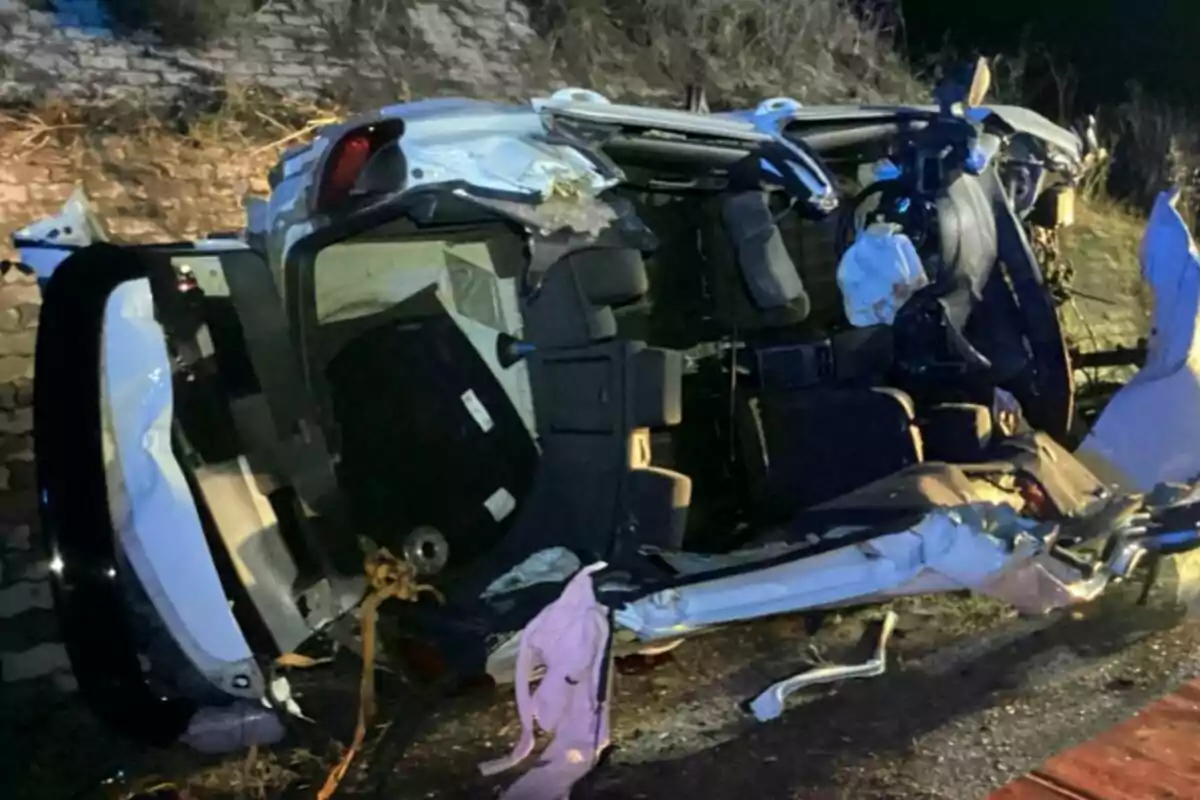 Un coche volcado y gravemente dañado en el borde de una carretera.