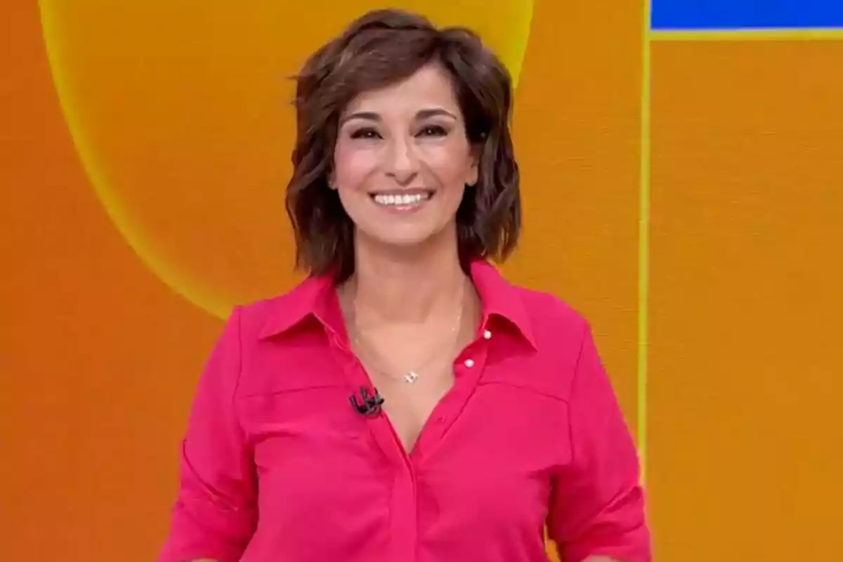 Adela González sonriendo con camisa rosa frente a un fondo naranja en Mañaneros