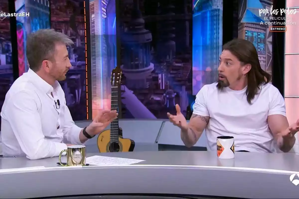 Pablo Motos y Adrián Lastra conversan en El Hormiguero, una de ellas gesticula con las manos mientras la otra escucha atentamente; hay una guitarra en el fondo y tazas sobre la mesa. Pablo Motos y Adrián Lastra conversan en El Hormiguero, una de ellas gesticula con las manos mientras la otra escucha atentamente; hay una guitarra en el fondo y tazas sobre la mesa.