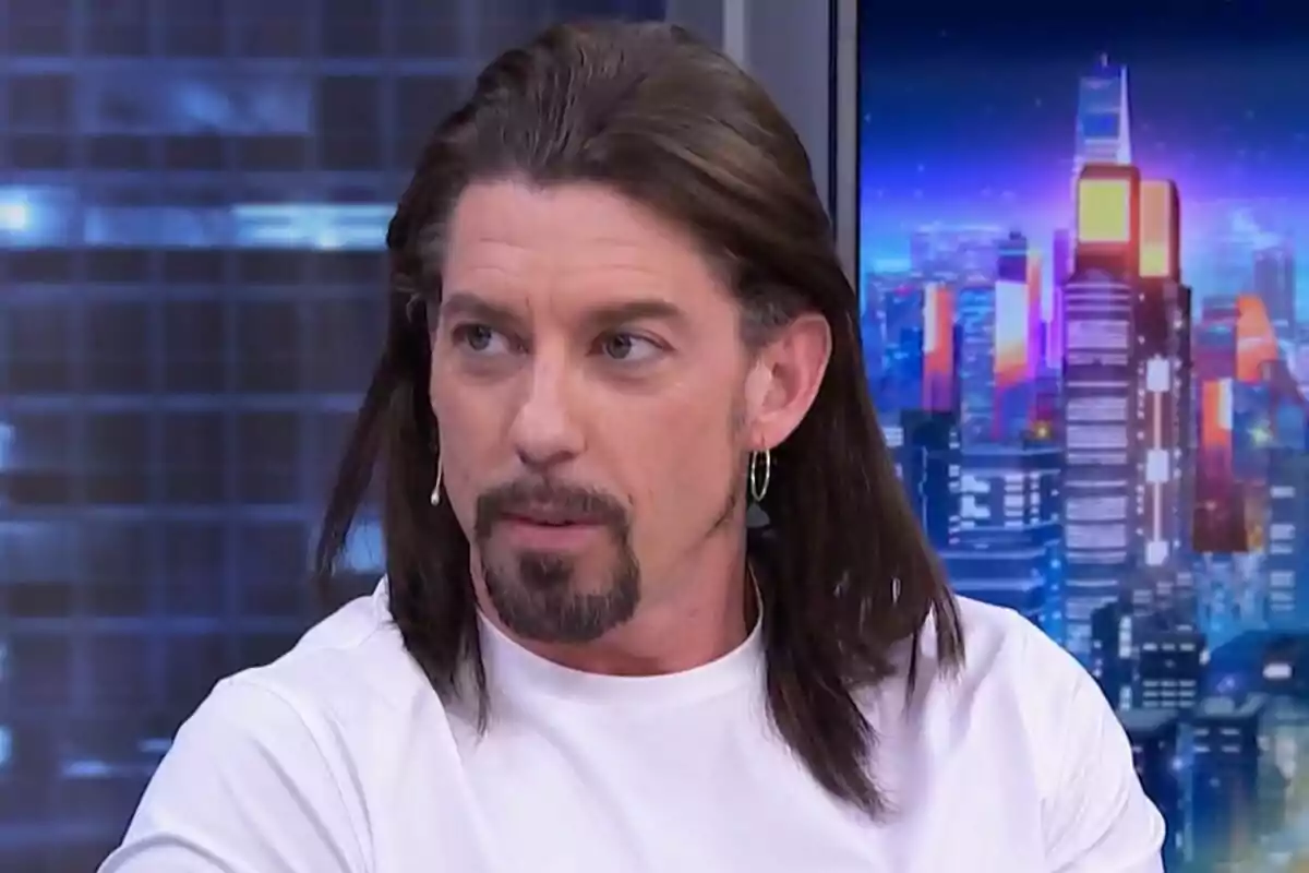 Adrián Lastra con cabello largo y barba está en El Hormiguero con un fondo de ciudad iluminada.