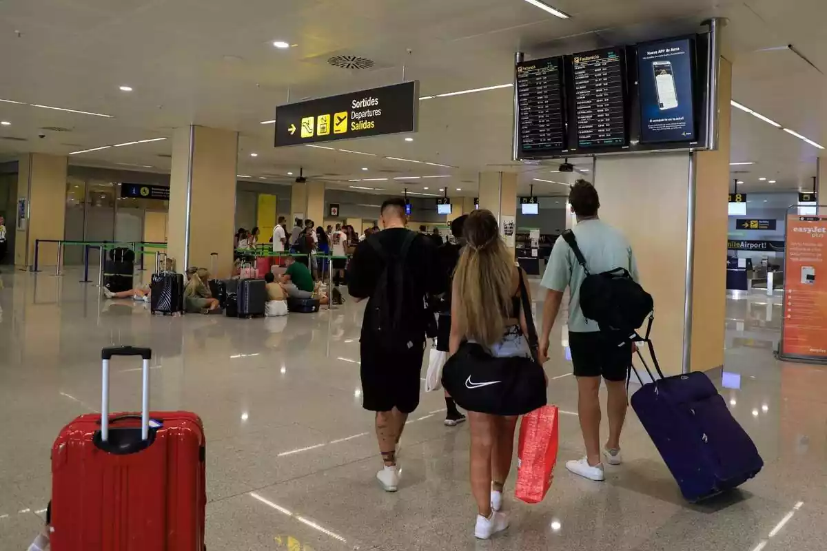 10 de agosto de 2023, España, Ibiza: La gente mira la pantalla de la terminal del aeropuerto de Ibiza