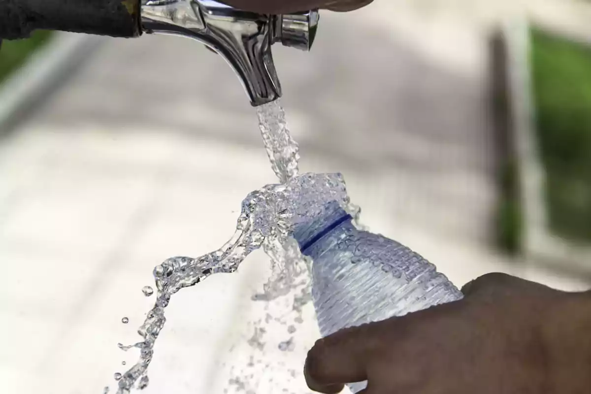 Una mano llenando una botella de plástico con agua de un grifo.