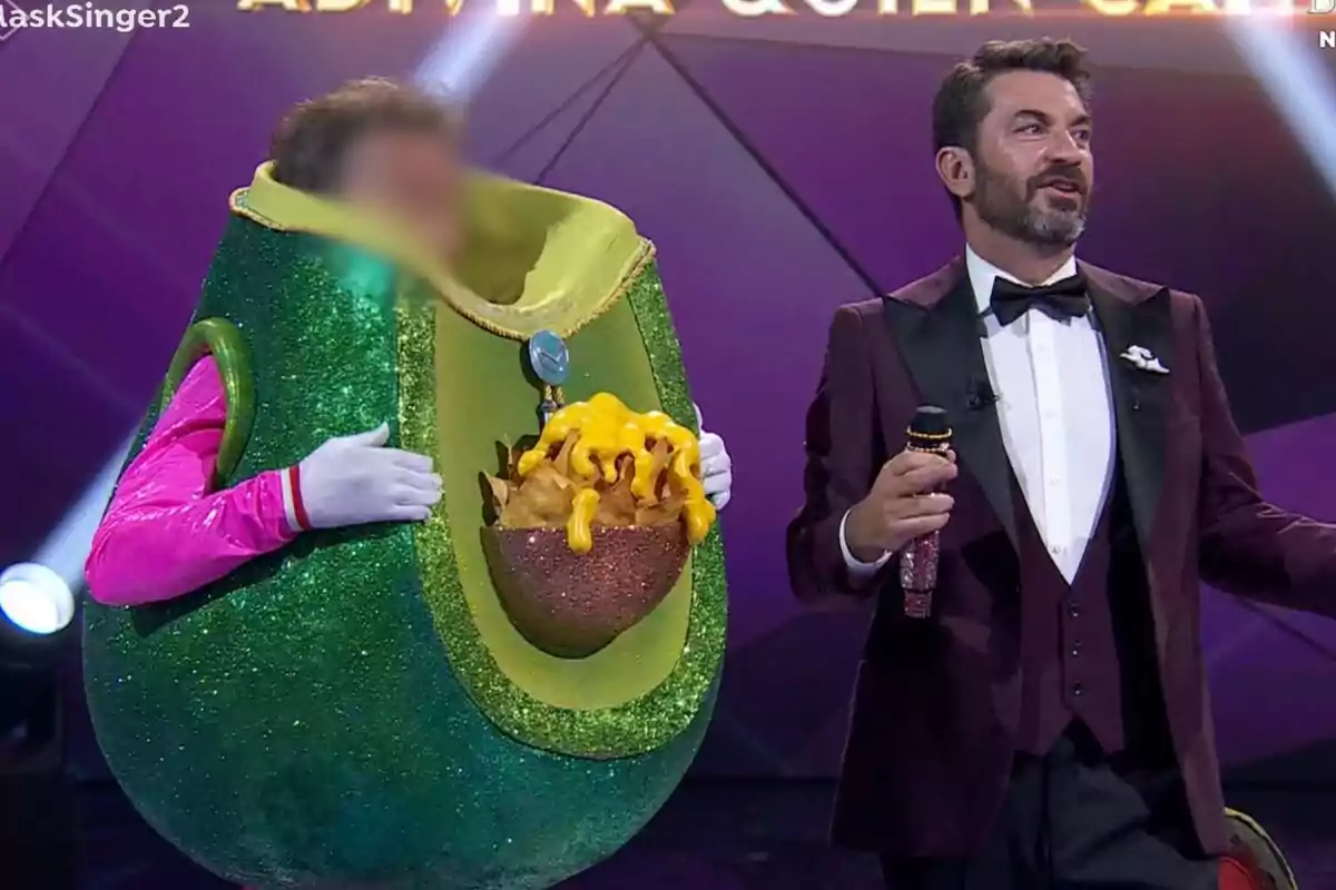 Una persona disfrazada de aguacate con nachos y queso con la cara pixelada junto a Arturo Valls en Mask Singer