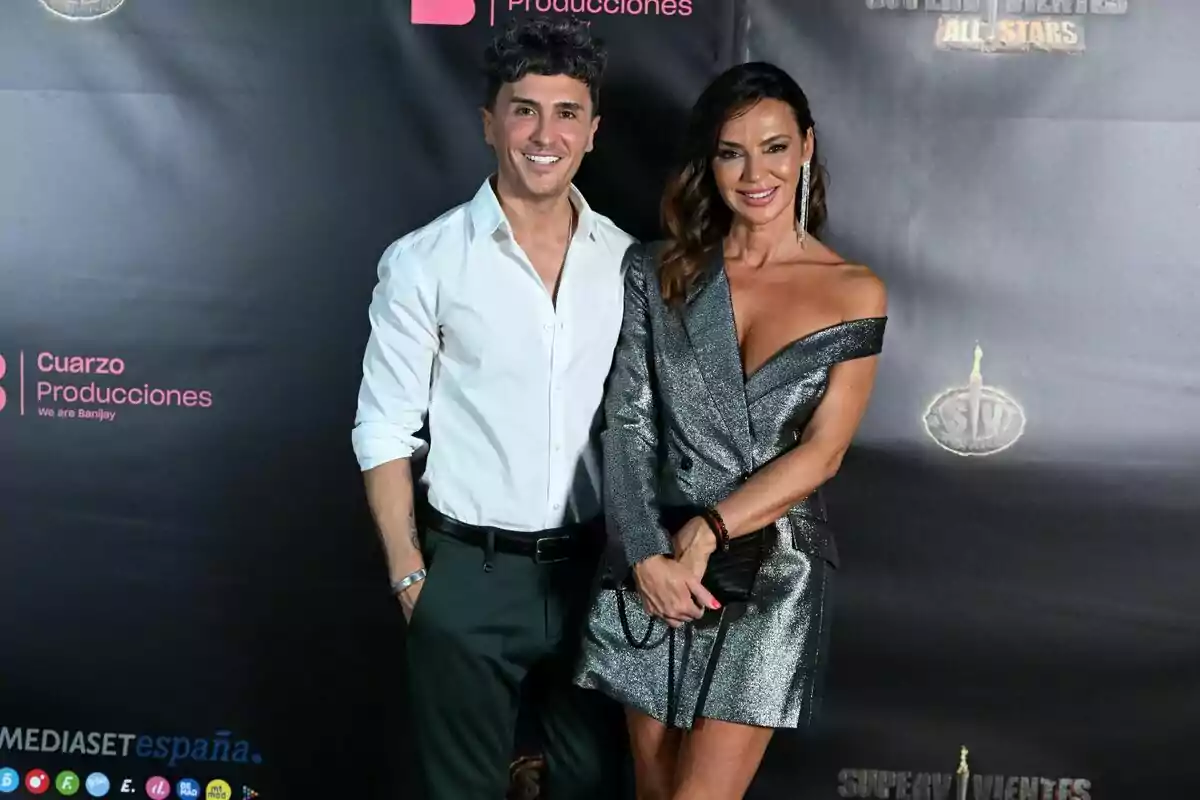 Agustín Etienne y Olga Moreno posan sonrientes en un evento, con un fondo que muestra logotipos de Cuarzo Producciones y Mediaset España.