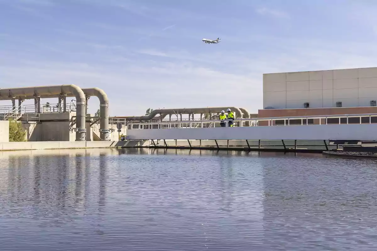 Vista de una planta de tratamiento de agua con trabajadores en un puente y un avión volando en el cielo.