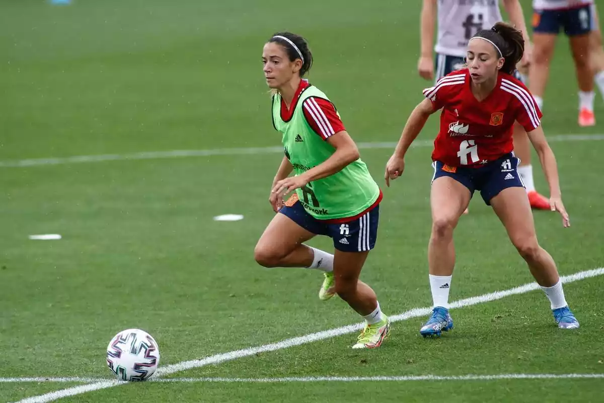 Aitana Bonmatí conduciendo la pelota al lado de Athenea del Castillo