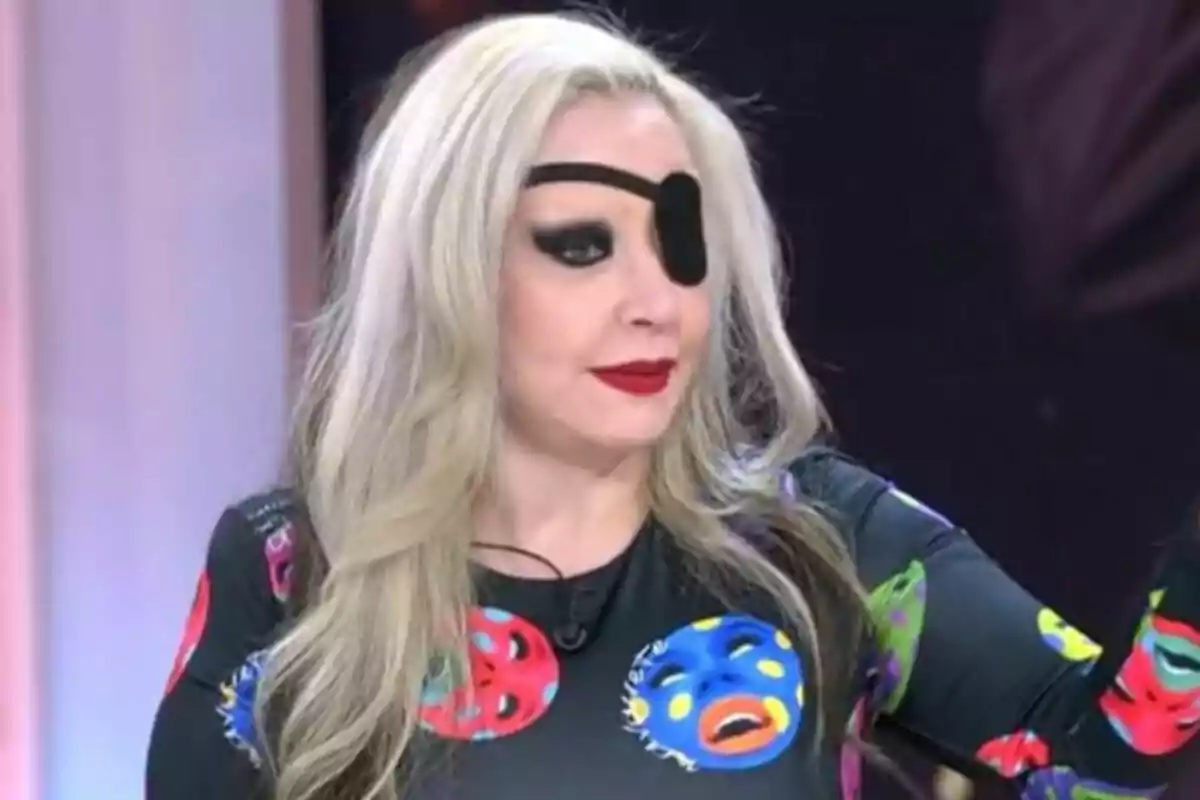 Alaska con cabello rubio y parche en el ojo, vistiendo una camiseta con estampados coloridos de caras en TardeAR.