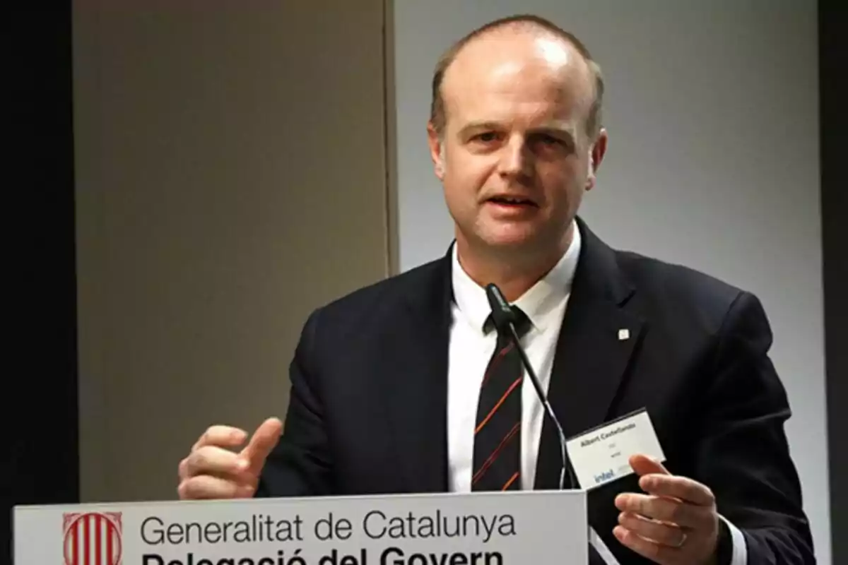 Hombre de traje hablando en un podio con un micrófono y un cartel de la Generalitat de Catalunya Hombre de traje hablando en un podio con un micrófono y un cartel de la Generalitat de Catalunya
