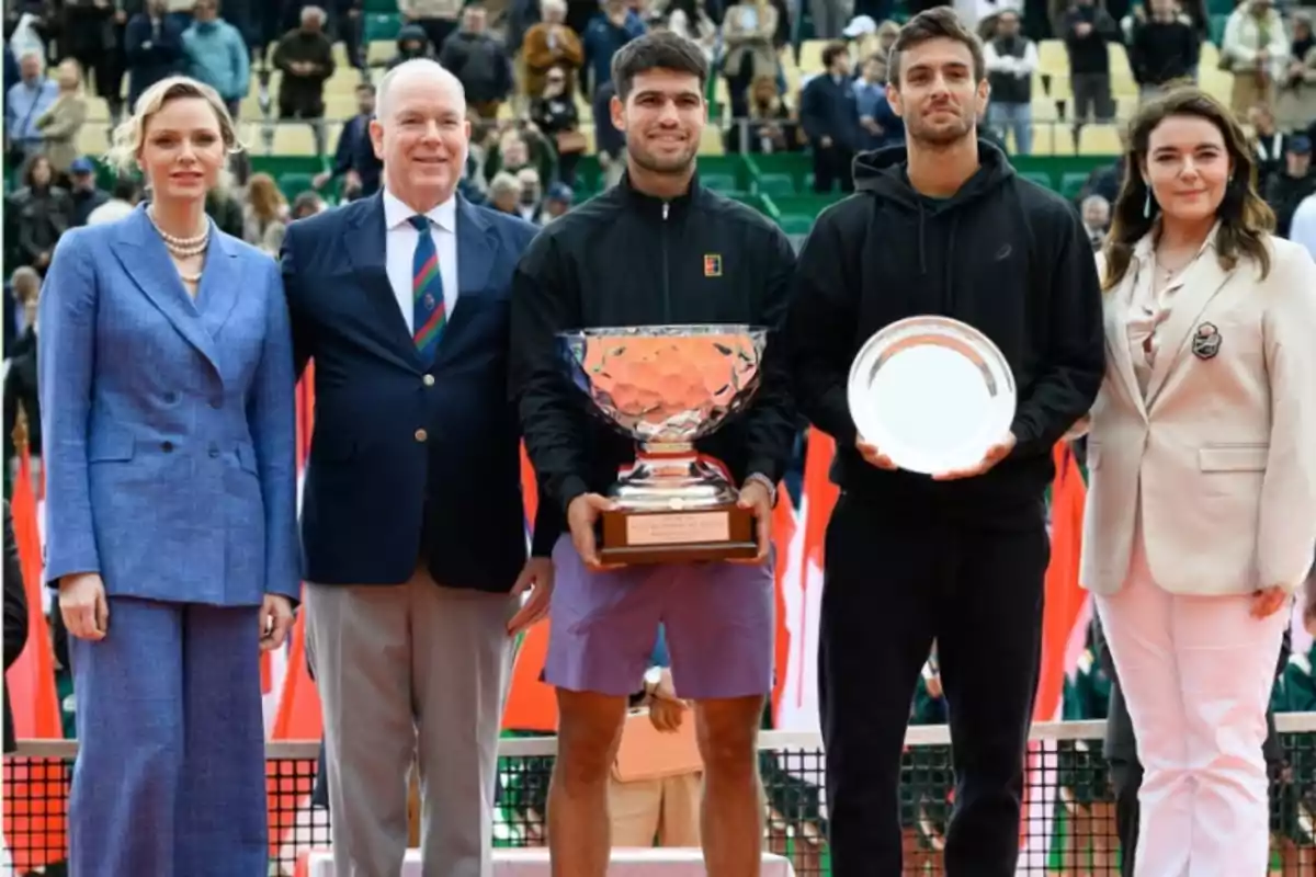 Un grupo de personas posando en una ceremonia de premiación de tenis, dos de ellos sostienen trofeos. Un grupo de personas posando en una ceremonia de premiación de tenis, dos de ellos sostienen trofeos.