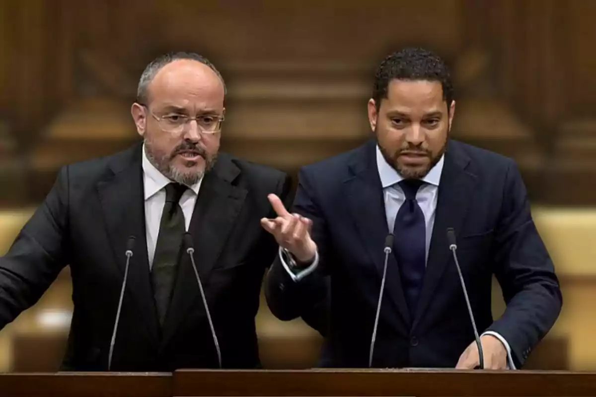 Dos hombres en trajes oscuros hablando en un podio con micrófonos frente a un fondo de madera.