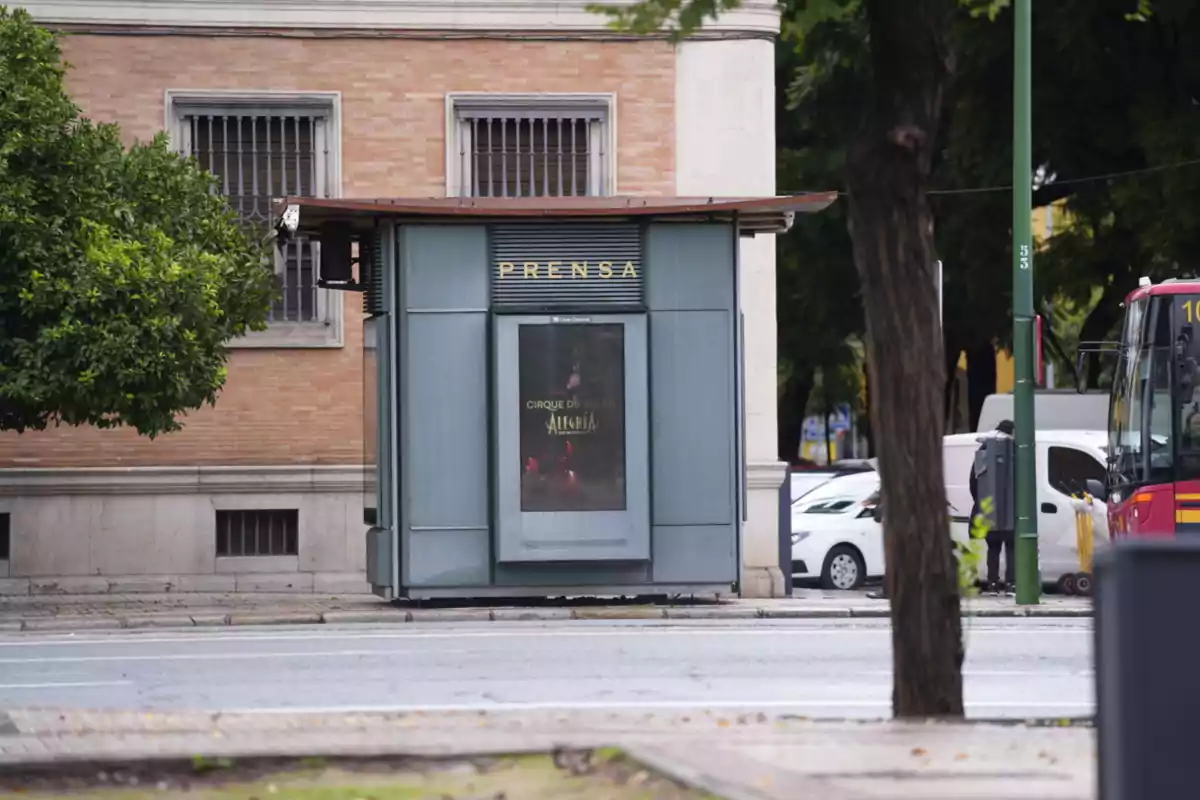 Quiosco de prensa en una calle con un cartel del Cirque du Soleil y un autobús rojo a la derecha.