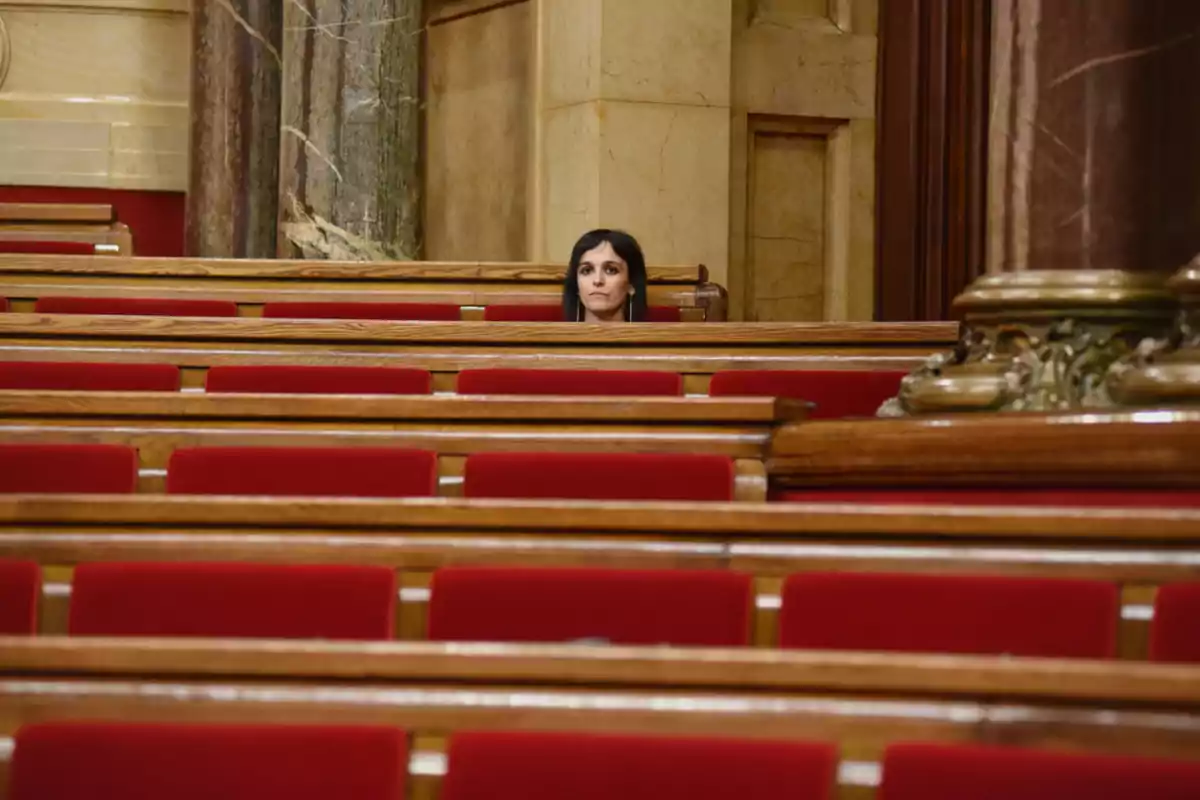 Una mujer sentada sola en un auditorio con asientos rojos y detalles de madera.