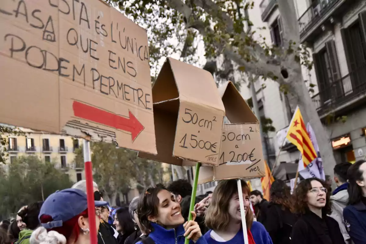 Personas en una manifestación sostienen carteles de cartón en forma de casa con mensajes sobre el alto costo de la vivienda.