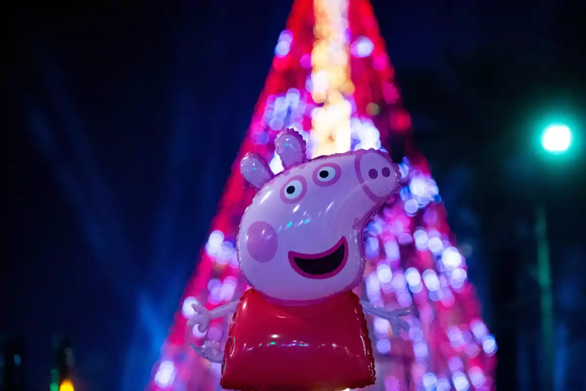 Un globo de personaje animado frente a un árbol de Navidad iluminado por la noche.