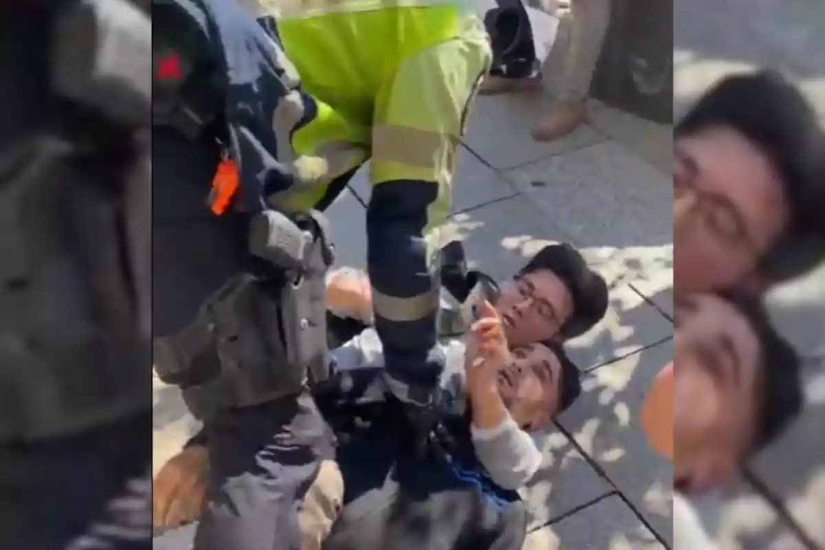 Un oficial de policía detiene a dos personas en el suelo durante un incidente en la calle.