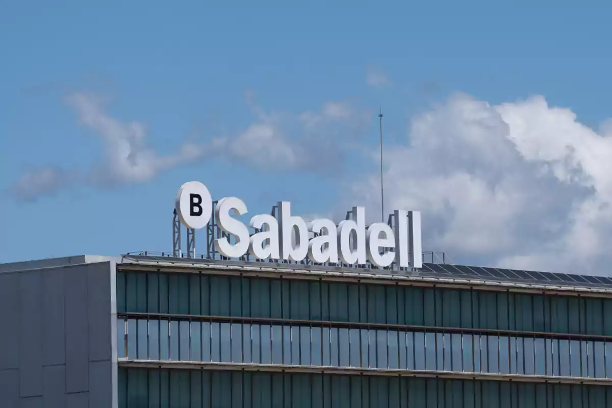 Edificio con el logotipo de Sabadell en la parte superior bajo un cielo azul con algunas nubes.