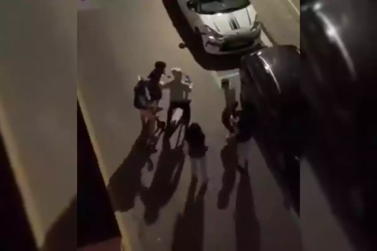 Un grupo de personas de pie en una calle junto a varios coches estacionados.