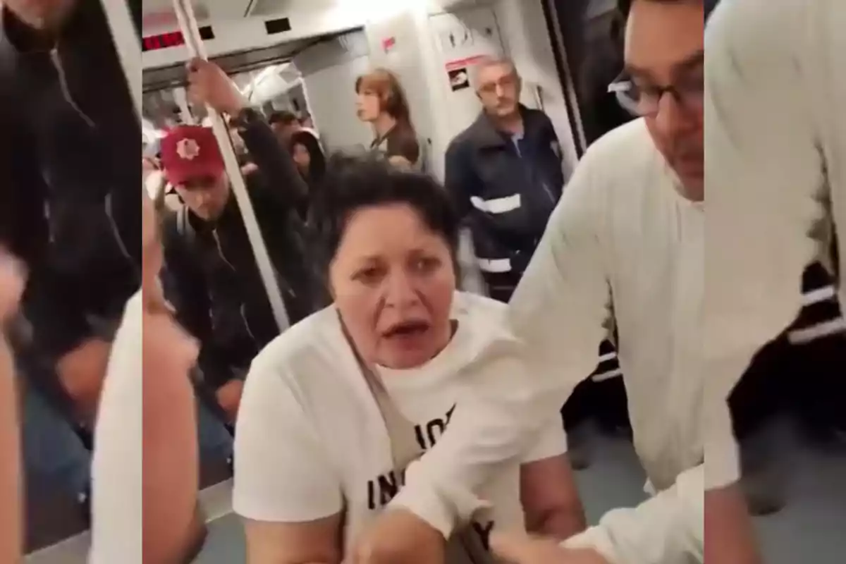 Una mujer con expresión preocupada está siendo asistida por un hombre en un vagón de metro lleno de pasajeros.
