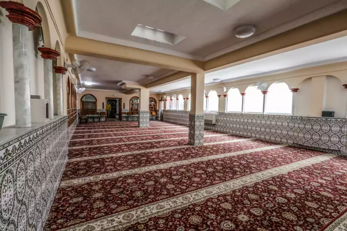 Interior de una mezquita con alfombras rojas y columnas decorativas