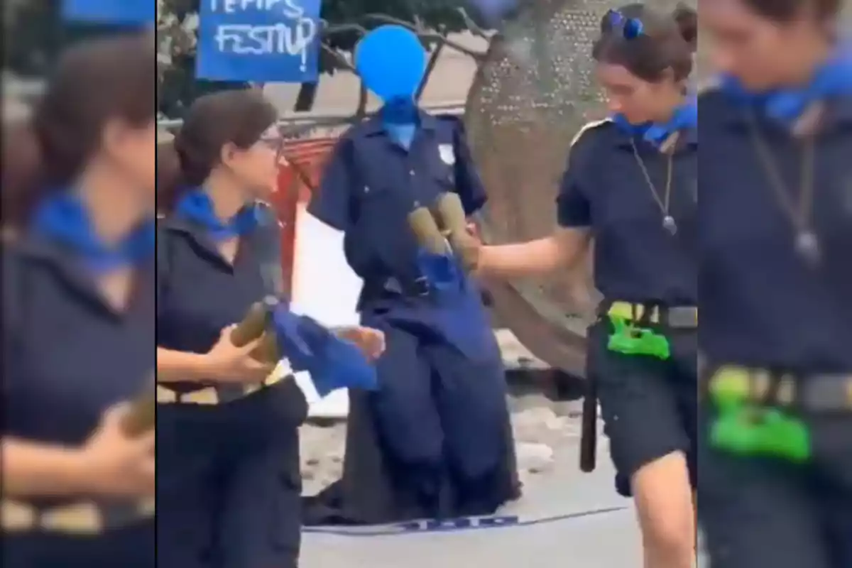 Dos personas vestidas con uniformes oscuros y pañuelos azules están participando en una actividad al aire libre, una de ellas sostiene objetos cilíndricos mientras la otra parece estar entregándole algo.