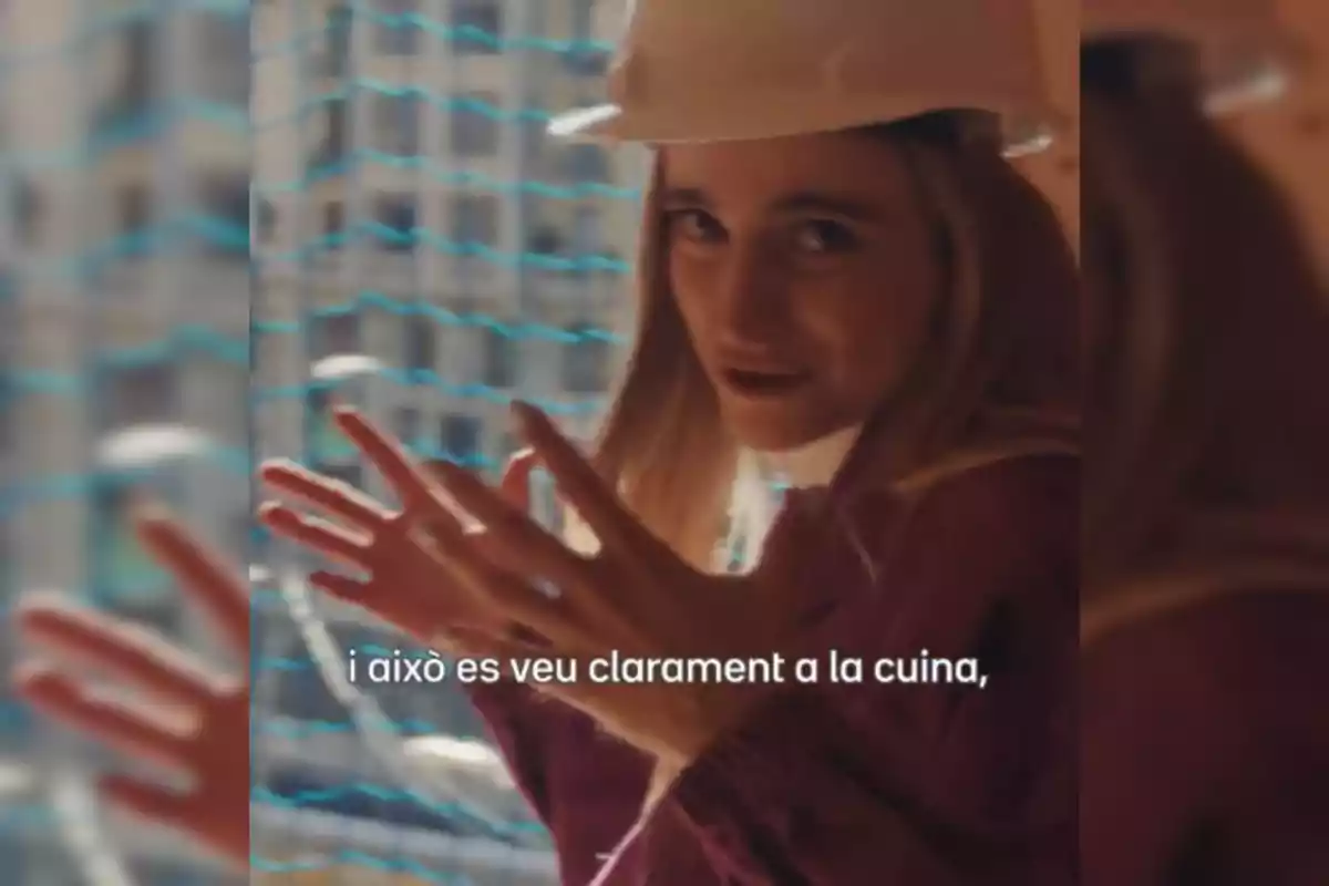 Mujer con casco de seguridad hablando y gesticulando frente a una red de protección en un entorno de construcción, con texto en catalán en la parte inferior.